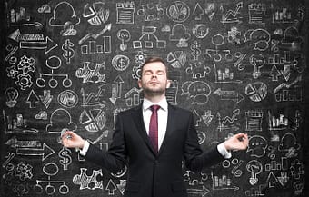 Businessman meditating in front of chalkboard with complex illustrations