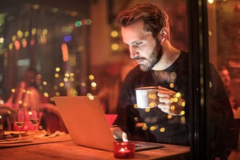 Man drinking coffee while working on his computer late at night
