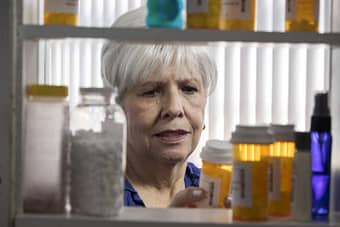 Older woman examines bottle of prescription medication pulled from medicine cabinet