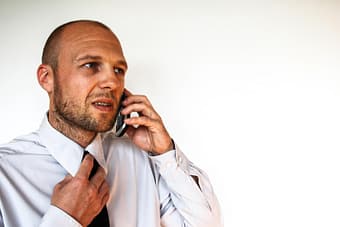 Worried man speaking on cell phone while loosening his tie