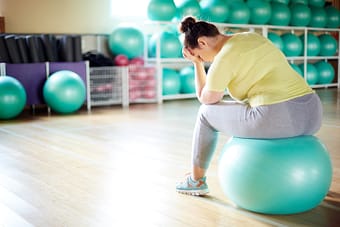 Distraught woman on yoga ball in workout studio