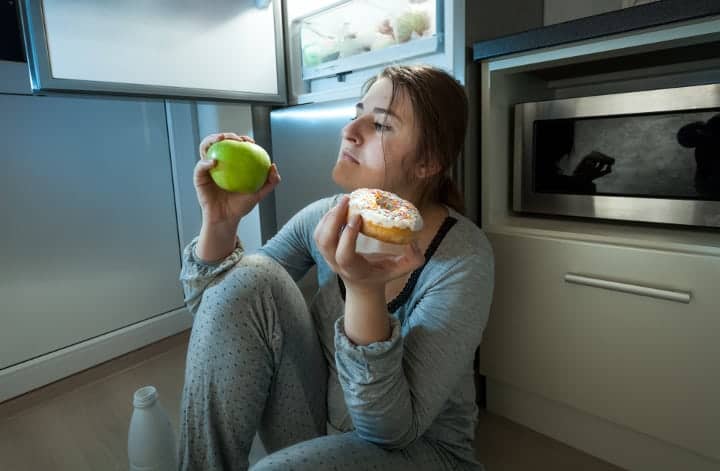 woman choosing between an apple and donut for a meal