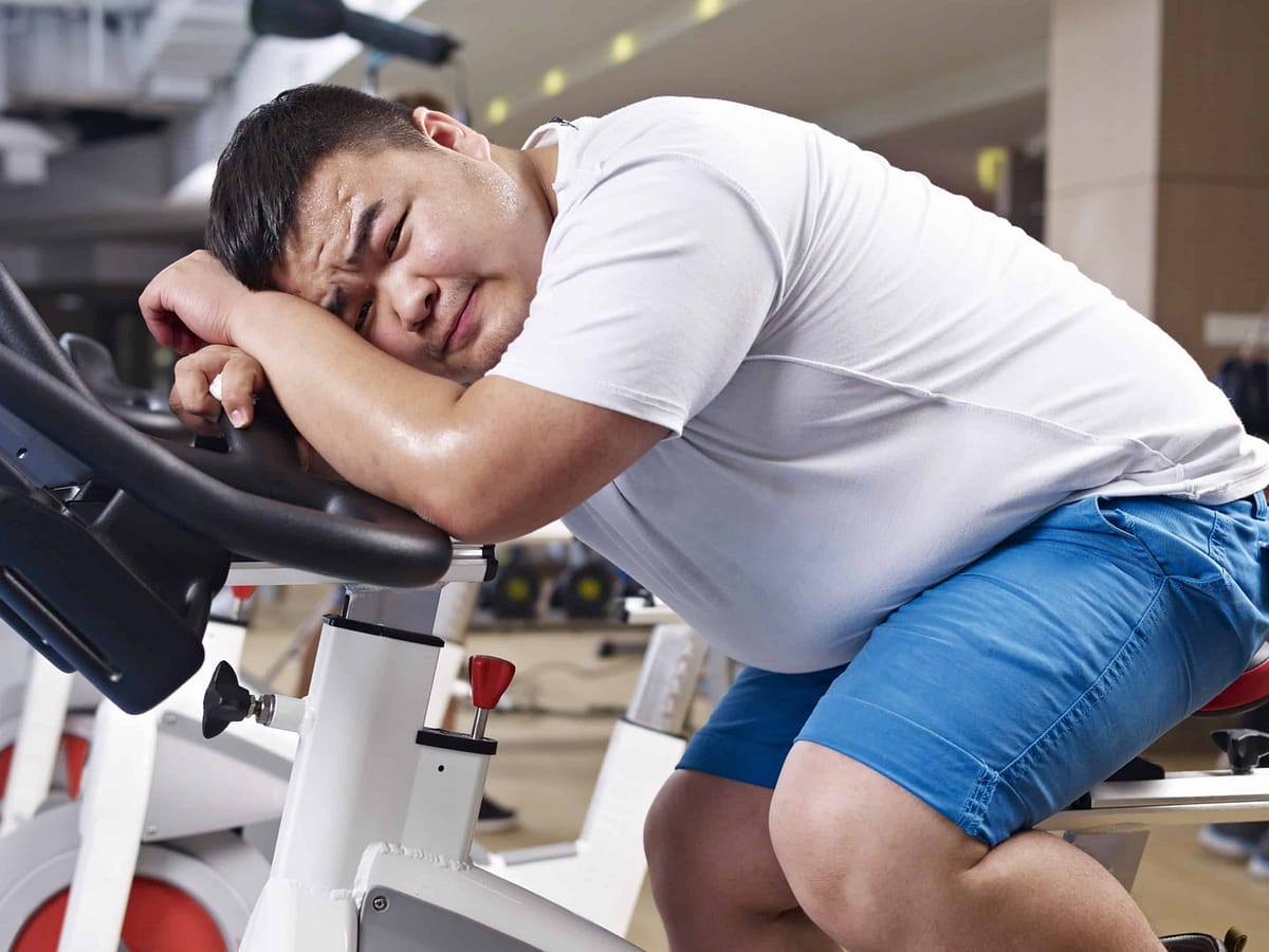 Exhausted, overweight male collapsed on exercise bike in gym