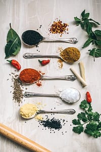 array of spoons filled with spices surrounded by herbs