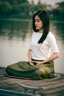 young woman doing relaxing deep breathing exercises on a dock