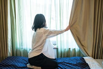 Woman drawing curtain next to bed before sleeping