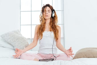 Woman meditating on bed with headphones on