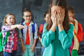 Young schoolgirl in tears getting mocked by her classmates