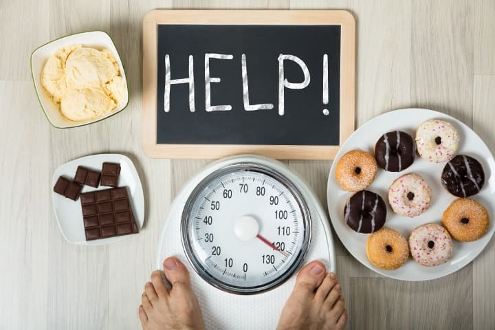 Man on scale tempted by sugary foods with sign for help