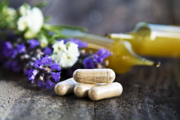 Herbal supplement capsules next to lavender flowers and ampules
