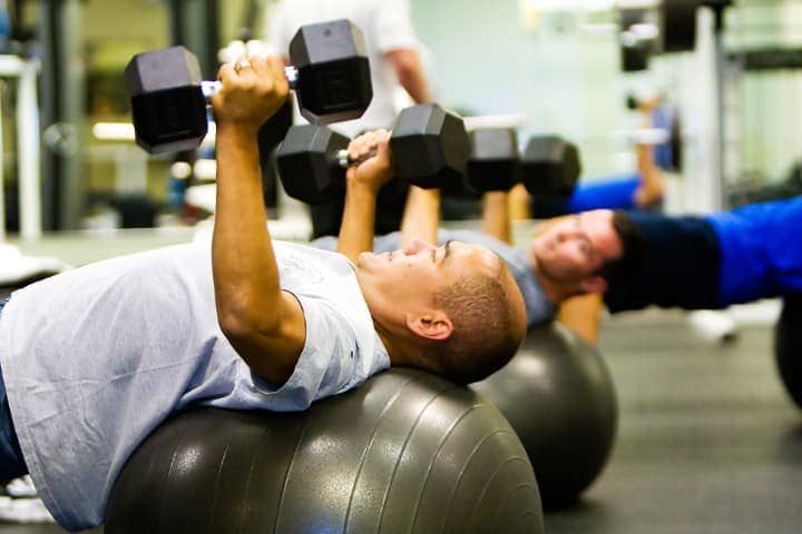 men lifting weights on balance balls in gym