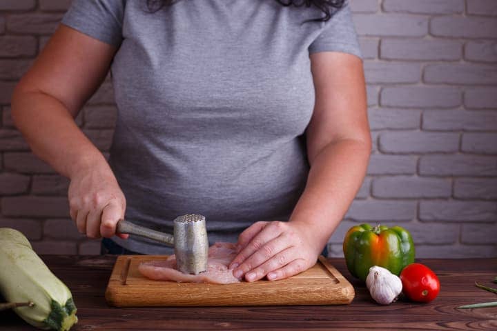 Overweight woman pounding chicken breast as part of LCHF diet