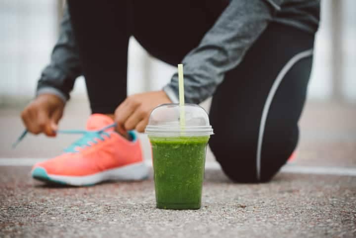 Runner tying his shoe laces next to green detox smoothie