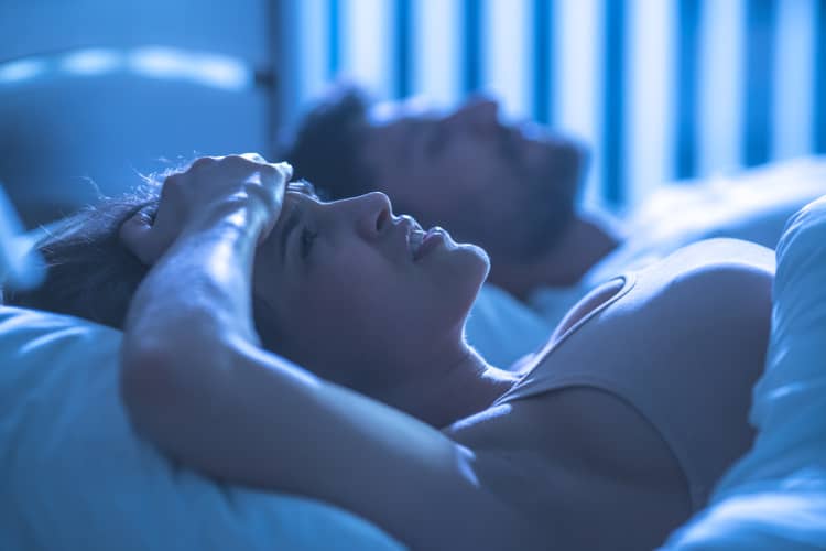 Women awake in bed next to sleeping partner