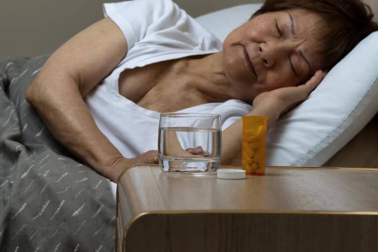 Asian woman sleeping with pills and glass of water next to bed