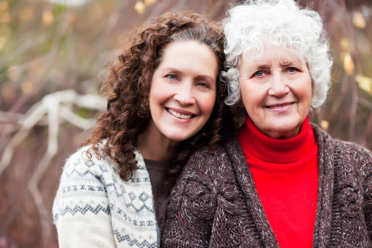 An adult daughter hugs her white-haired mother