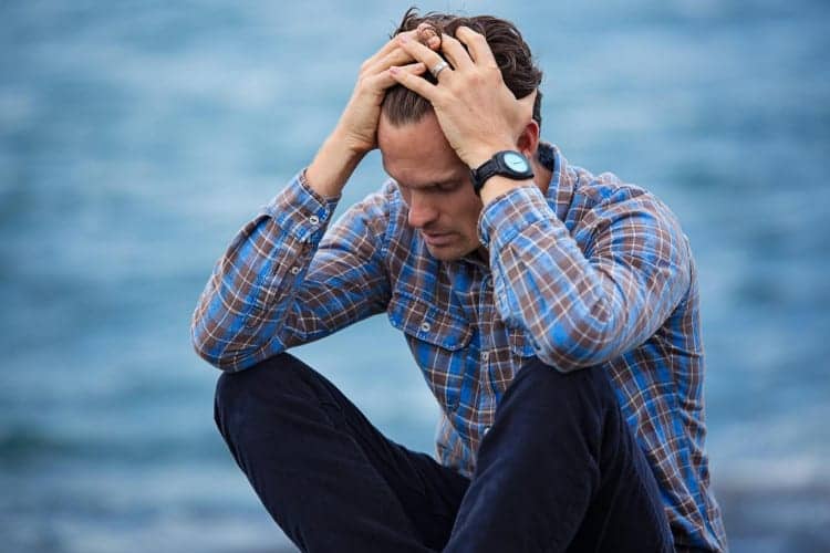 Sad man holding his head in his hands by the shore