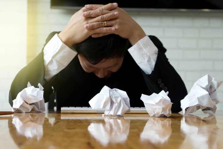 Frustrated man with head in hands surrounded by crumpled papers