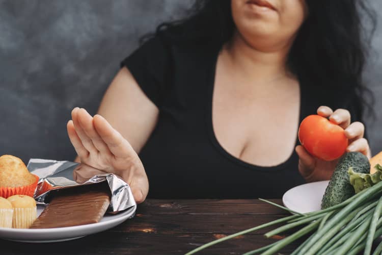 Overweight woman pushing away snacks in favor of vegetables