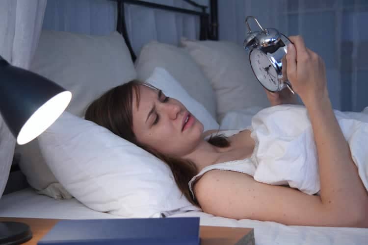 Awake woman looking anxiously at alarm clock in the middle of the night