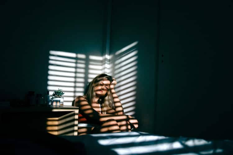 Exhausted woman crouching in corner of darkened room