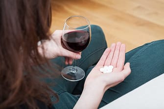 Woman holding a glass of red wine and white sleeping pills