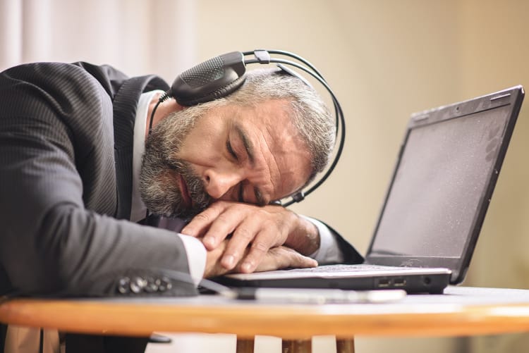 Grey-haired businessman resting on laptop with listening to hypnosis audio on headphones