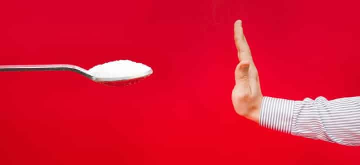 hand pushing away spoonful of refined sugar