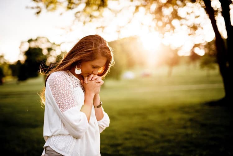Young woman prayerfully giving gratitude in field at sunrise